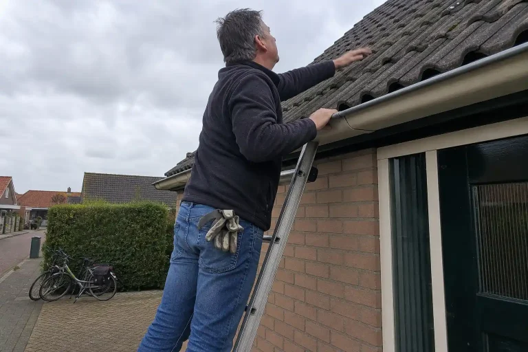 Person på stege inspekterar taktegel inför att byta eller renovera tak på villa en mulen dag.