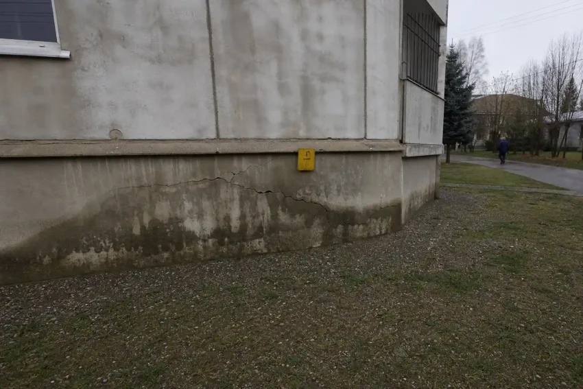 Sprickig betonggrund med fuktfläckar och en gul varningsskylt, fuktskador i grunden varningstecken syns tydligt.