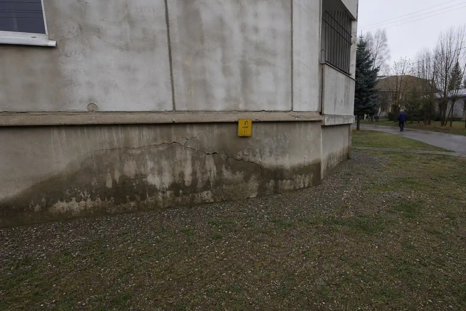 Sprickig betonggrund med fuktfläckar och en gul varningsskylt, fuktskador i grunden varningstecken syns tydligt.
